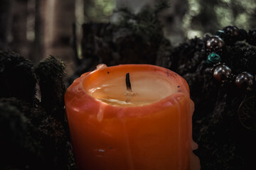 red extinguished candle with wax, a symbol of the moon, an amulet lying on moss on a dark natural...