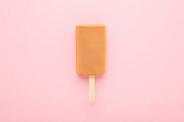 Light brown caramel ice cream on stick on light pink table background. Pastel color. Closeup. Top...