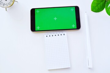 Smartphone green screen mockup and black pen with notepad. Technology concept of notepad, pen and smartphone. blogger in summer