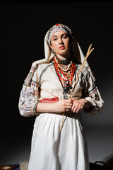 young ukrainian woman in traditional clothing with ornament holding wheat spikelets on black.