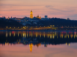 Naklejka premium Kiev-Pechersk Lavra and city lights. Silhouette panorama at sunset of the colorful sky over the Dnieper river with passing ducks in Kyiv