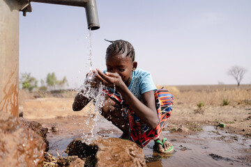Little African girl splashing herself with copious amounts of clean water at a freshwater well...