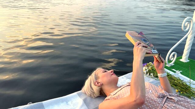 A blonde girl lies on a raft and reads a book 