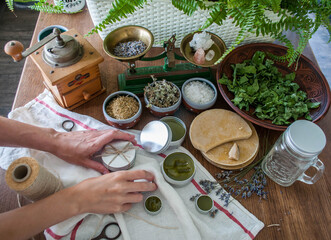 Women's hands holding a tin jar of homemade salve. Home herbalism and cosmetics. Natural homemade salve in metallic tin jar with dried plants and herbs flowers.