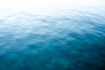 Blue water surface. Turquoise sea waves. Transparent sea water with rocks on bottom. Defocused image for background. Waves texture. Blurred image