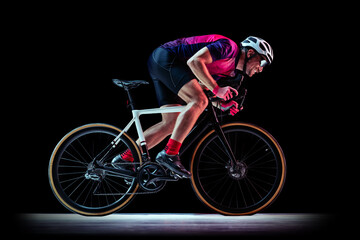 Portrait of man, professional cyclist training, riding isolated over black studio background in neon light