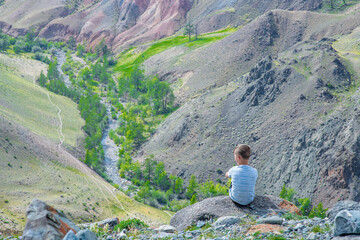 Little happy boy enjoys the view of the mountains and river. Empty space for text