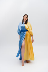 full length of barefoot young ukrainian woman in blue and yellow dress posing on grey.