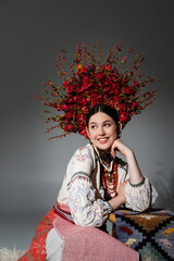 happy ukrainian woman in traditional clothes and floral red wreath on grey.
