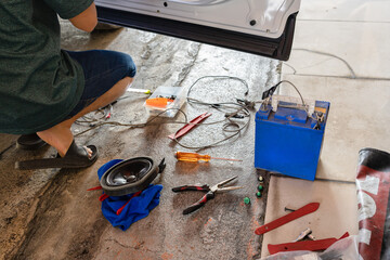 Mechanic man fixing the car with speaker equipment, pliers, wire and battery in workplace
