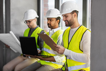 architecture, construction business and people concept - group of male architects in helmets with laptop, blueprint and clipboard working at office