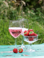Two glasses of rose sparkling wine and strawberry on a  table. Romantic picnic outdoors. Close up photo of glass tableware. Summer drinks and food. 