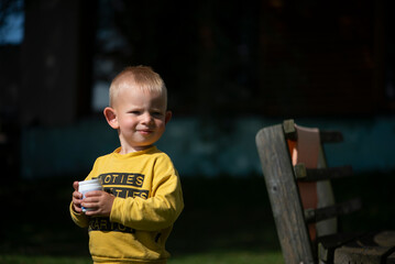 Portrait of little boy wearing yellow sweater standing outddors in ssunny summer day