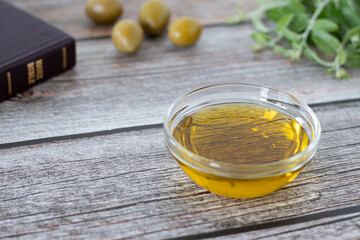 Extra virgin olive oil in a glass container with a closed Holy Bible Book, green olive branch, and...