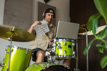 Young man conducts drum lesson via laptop. Guy starts lesson by greeting followers and shows music sheet. Drummer explains concept of playing drums technique