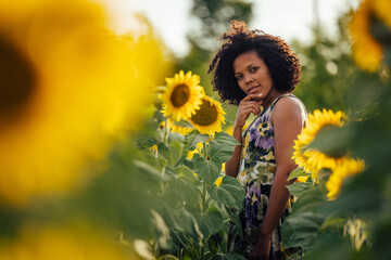 Portrait of a serious-looking woman, posing for the camera, standing in the field of sunflowers.