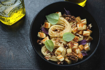 Black bowl with halloumi cheese and walnuts spaghetti, horizontal shot on a dark-brown stone background, middle close-up