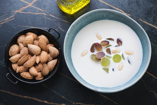 Bowl of ajoblanco or spanish white gazpacho served with grapes, elevated view on a dark-olive marble background