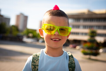 Cute smiling baby boy with bright green glasses outdoors in sunny weather.