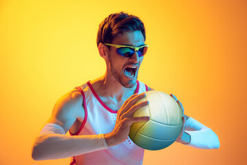 Portrait of young man, beach volleyball player posing isolated over yellow studio background in neon light. Motivation