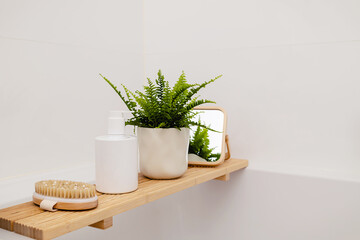 Bathtub wooden tray with white beauty cosmetic bottle and accessories in a modern interior scandinavian bathroom with white tiles as a background with copy space. Home decor with and green plant..