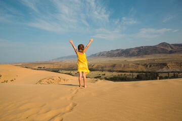 A tourist girl in a yellow dress runs along a sandy dune in the desert. Travel, sights of Dagestan, Sarykum dune