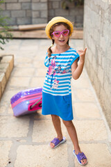 A girl with a suitcase, a hat and sunglasses is going on vacation. Waiting for the trip, arrival at the place of residence at the hotel.