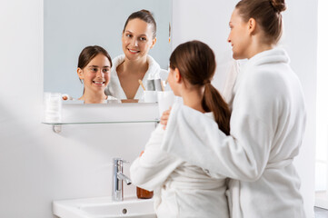 beauty, hygiene, morning and people concept - happy smiling mother and daughter looking to mirror at bathroom