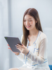 Fototapeta premium Professional young age Asian business woman with long hair in white shirt holds tablet her smiling happily while she sits on chair in workplace office.