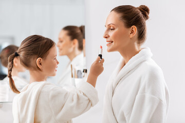 beauty, family and people concept - happy smiling mother and little daughter with lipstick applying make up in bathroom