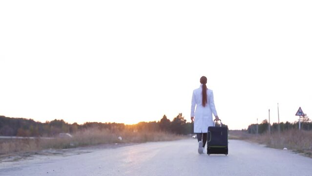 a lonely woman with a suitcase is walking on an empty road, the concept of travel, to be in an unknown place alone.