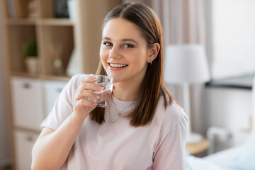 health and people concept - happy smiling girl with glass drinking water at home