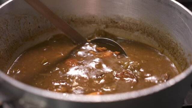 Ladle stirs chicken sausage gumbo, traditional Louisiana cajun dark roux gumbo, close up slow motion 4K