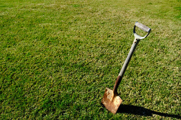 An old rusty spade with a weathered wooden handle is dug into a lawn