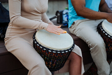 The girl plays the drum djembe together with other people, street musicians beat the rhythms of...