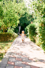 Fototapeta na wymiar Little girl runs along the paving stones in a green park