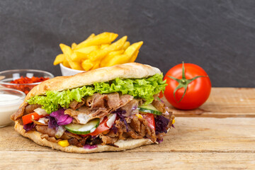 Döner Kebab Doner Kebap fast food meal in flatbread with fries on a wooden board and copyspace...