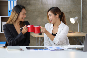 Businesswoman and coworker happily working together and drinking coffee in the office in the morning.