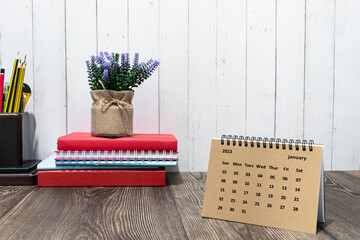 Brown January 2023 calendar on wooden desk with office stationery.