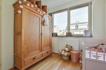Interior of white room with baby crib and armchair near window with blue chest of drawers in...