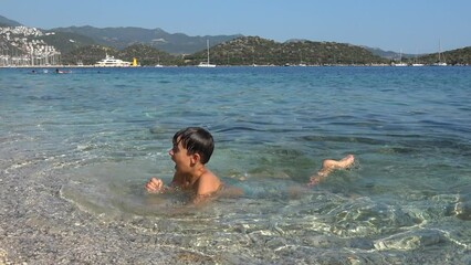 Kas, Turkey - 2nd of July 2022: 4K Cute artistic boy splashes and dives in the crystal clear sea
