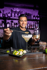 smiling waiter depositing a lime into a cocktail at a bar counter