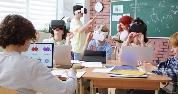 Elementary school age children sitting in VR glasses and learning to use virtual reality with help of teacher during chemical lesson. Concept of modern technology in education.