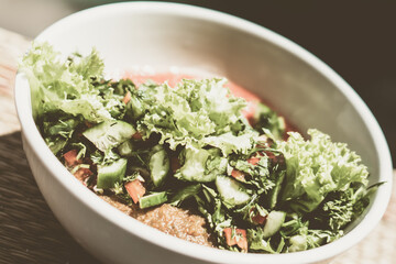 Ceramic white light bowl with mix green lettuce leaves, spinach leaf salad ingredients fresh vegetables pureed red tomato serving plate. Healthy vegan food cuisine. Close-up View from above
