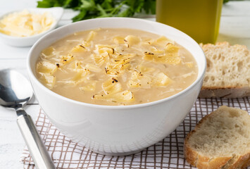 Onion soup with cheese in a bowl with bread slices and seasonings over wooden table