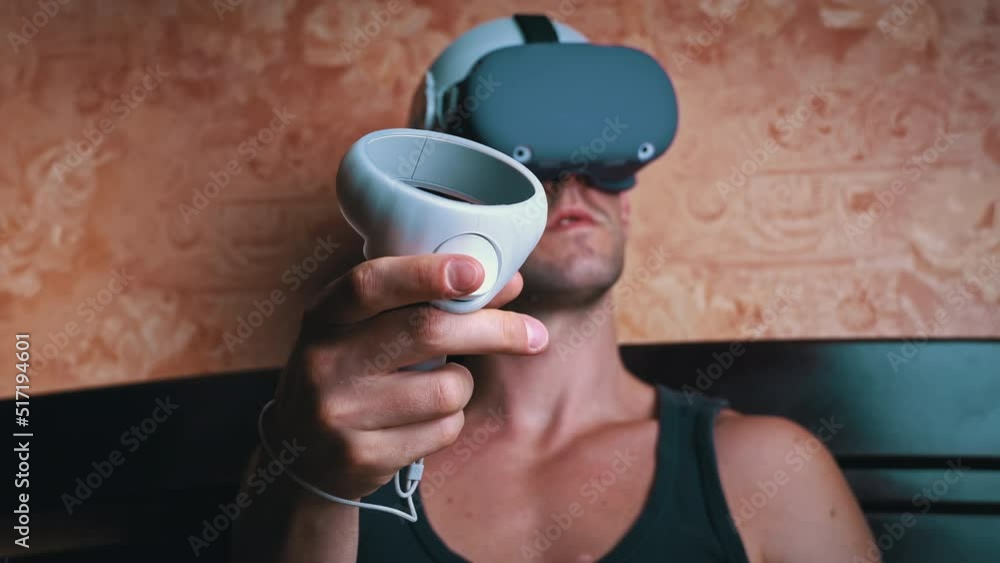Poster man in a virtual reality helmet controls the controllers. a young man at home sitting on a bed is in
