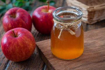 Apple cider vinegar in glass bottle and fresh red apples on wooden table