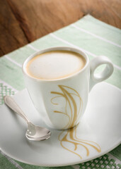 Ceramic cup of expresso with an illustration, on a green placemat on a wooden table