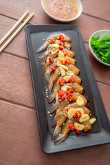 Prawns pickled in soy sauce or shoyu sauce and sprinkled with chili and sliced garlic with spicy sauce Seaweed and Japanese rice are side dishes on a brown wooden table.