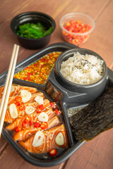 Salmon pickled in soy sauce or shoyu sauce and sprinkled with chili and sliced garlic. with spicy sauce Seaweed and Japanese rice are side dishes on a brown wooden table.